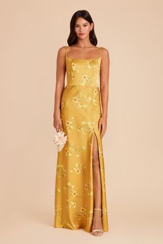 a woman wearing a yellow floral print dress with a slit down the side and one leg