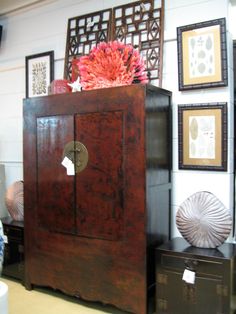 a wooden cabinet sitting in the middle of a room with pictures on the wall behind it