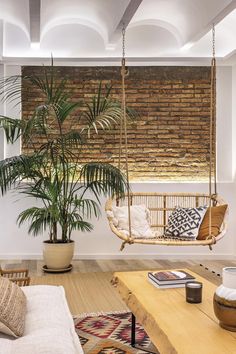 a living room filled with furniture and a hanging chair next to a plant on top of a wooden table