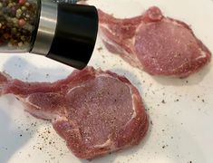 raw meat being seasoned on a plate with seasoning sprinkles and pepper