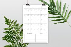 a printable calendar is hanging on a clipboard next to a green fern leaf