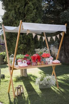 a wooden stand with flowers and decorations on it in the grass next to a tree