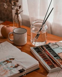 a wooden table topped with an open book next to a glass vase filled with flowers