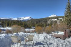 two chairs sitting in the snow next to a hot tub and trees with mountains in the background