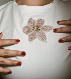 a woman with her hands on her stomach wearing a t - shirt that has an embroidered flower on it