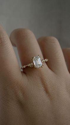 a woman's hand with a diamond ring on top of her finger and an emerald stone in the middle