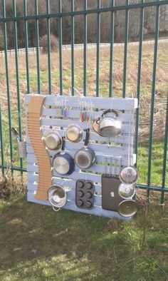 a metal rack with pots and pans hanging on it's side next to a green fence