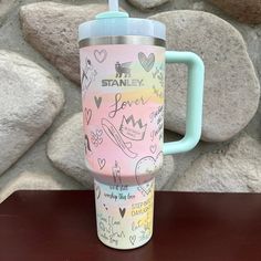 a pink and blue travel mug sitting on top of a table next to some rocks