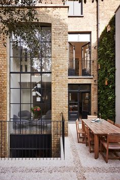 an outdoor dining area with wooden table and chairs, surrounded by brick walls that have plants growing on them