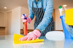 a woman in an apron and pink gloves is cleaning the floor with a yellow mop