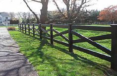 a wooden fence in the grass next to a tree and road with houses in the background