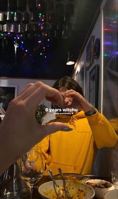 a woman in a yellow jacket is eating food at a table with two hands on her face