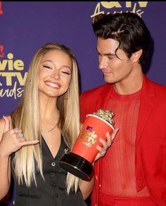 a man and woman standing next to each other holding a popcorn cup in their hands