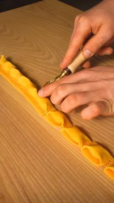 a person is using a knife to cut something yellow on a wooden table with wood grain