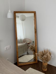 a mirror sitting on top of a wooden table next to a vase with dried flowers