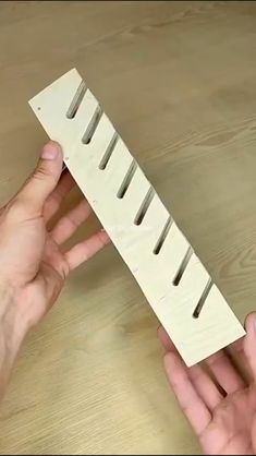 two hands are holding a piece of wood that is shaped like a long strip with holes in it