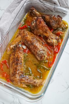 two chicken legs in a casserole dish with red peppers and green peppers on the side