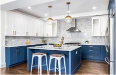 an open kitchen with blue cabinets and stools on the countertop, along with two pendant lights