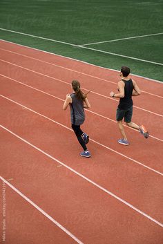 two people running on a track with one holding a tennis racquet and the other looking at something