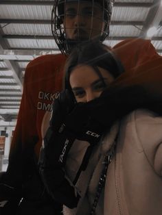 two people standing next to each other in a building with a goalie's helmet on