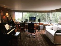 a living room filled with lots of furniture and a piano in front of a large window