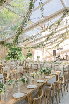 the tables are set up for an outdoor wedding reception with greenery hanging from the ceiling