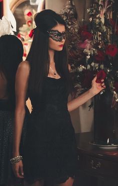 a woman in a black dress and blindfold holding a rose with her right hand