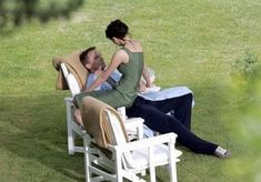 a man and woman sitting on lawn chairs in the grass, one is holding his head