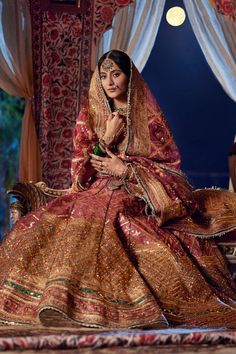 a woman sitting on top of a bed in a red and gold wedding dress,