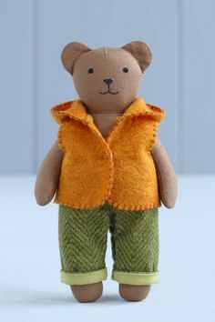 a small teddy bear wearing green pants and a yellow shirt is standing on a white surface