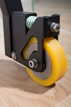 a close up of a yellow wheel on a wooden table with a black handle and two screws