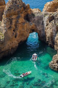 two boats are in the clear blue water near some rocks and an arch shaped rock formation