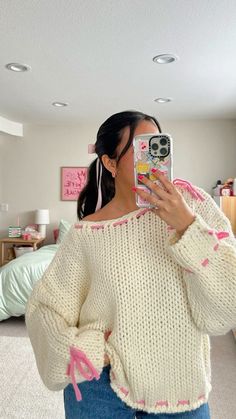 a woman taking a selfie with her cell phone while wearing a sweater and jeans