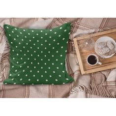 a green pillow with white polka dots on it next to a cup of coffee and tray