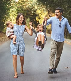 a man and woman walking down the street with two small children in their arms while holding hands