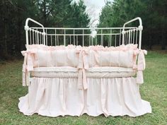 a white crib with pink ruffled bedding in the middle of a field