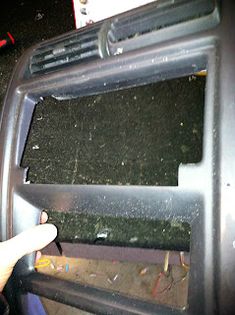 the inside of a car dashboard with debris all over it and a hand pointing at an electronic screen