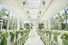 a bride standing in the middle of a long aisle with greenery on both sides