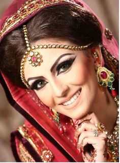 a woman in a red and gold outfit with jewelry on her head, smiling at the camera