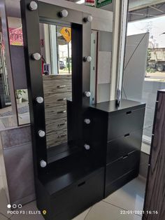 a black dresser with drawers and mirror in front of a large window at a store