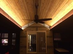 a ceiling fan mounted to the side of a wooden building with lights shining on it