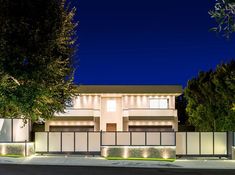 a modern house lit up at night with lights on the side and trees in front