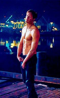 a shirtless man standing on a dock at night