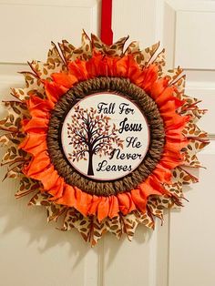 a wreath with an orange ribbon hanging from the front door that says, fall for jesus we never leaves