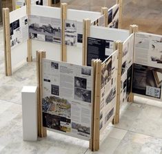 several pieces of newspaper on display in a room with white walls and wooden posts around them