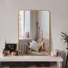 a mirror sitting on top of a white table next to a couch and potted plant