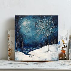 a painting is displayed on a shelf next to other art pieces, including one with a tree in the snow