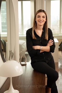 a woman sitting on top of a wooden table in front of a mirror and lamp