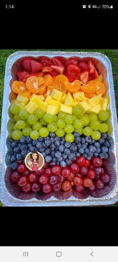 a tray filled with lots of different types of fruit on top of green grass next to a field