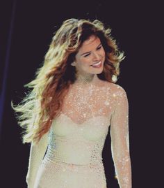 a woman with long hair wearing a white dress and smiling at the camera while standing in front of a microphone